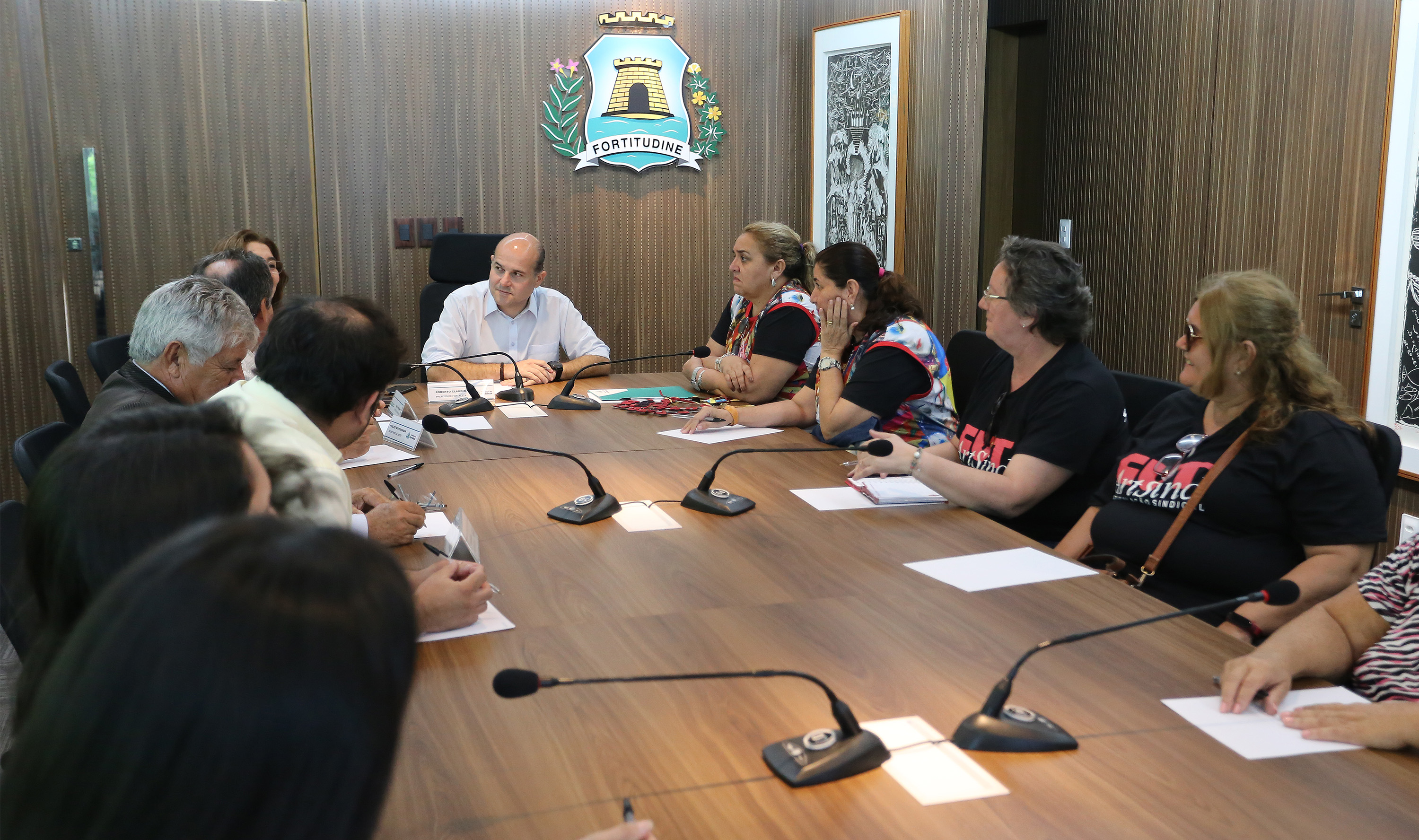 Prefeito sentado à mesa ao lado de pessoas sentadas ao redor